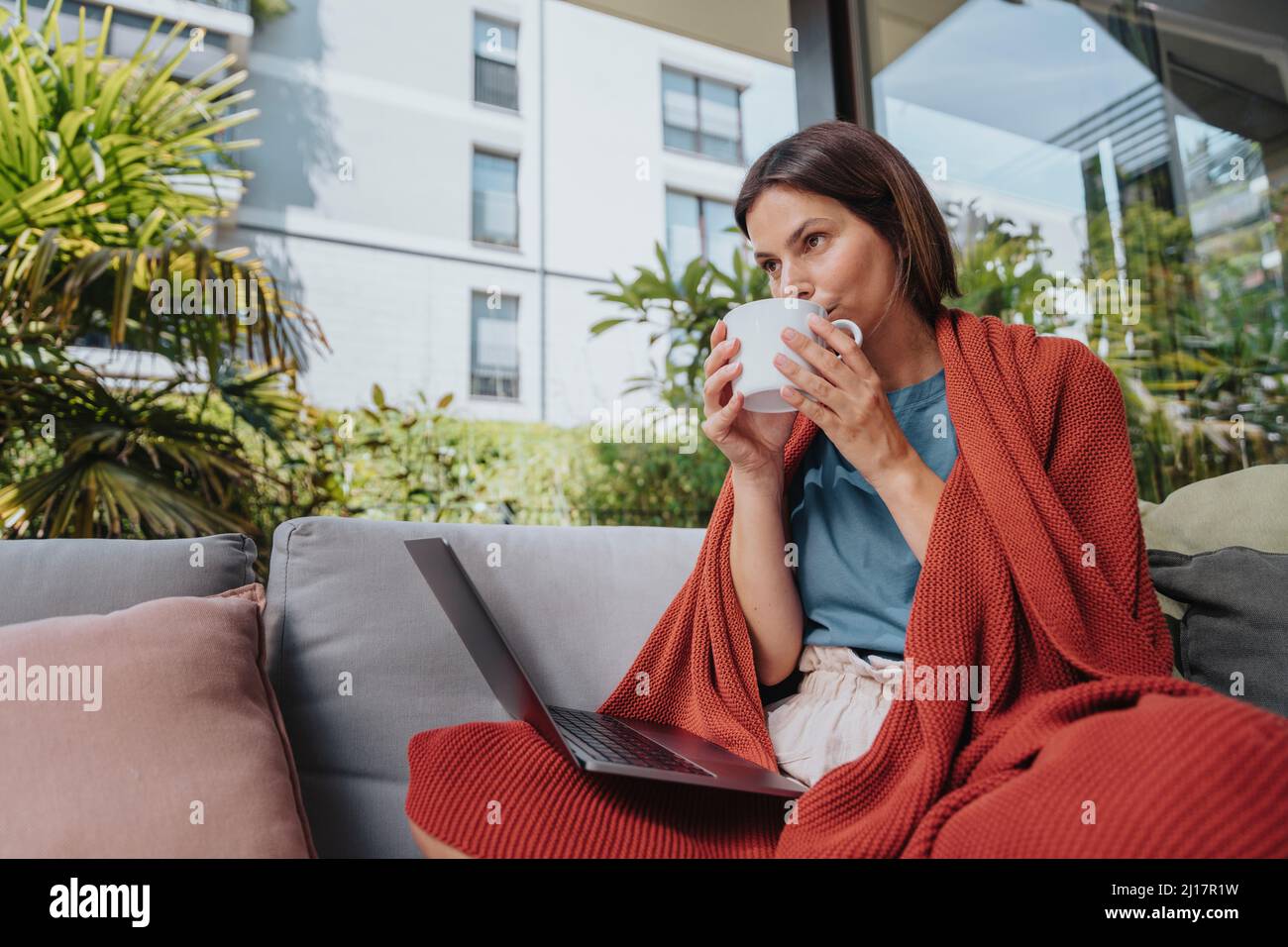 Freelancer with laptop drinking coffee at yard Stock Photo