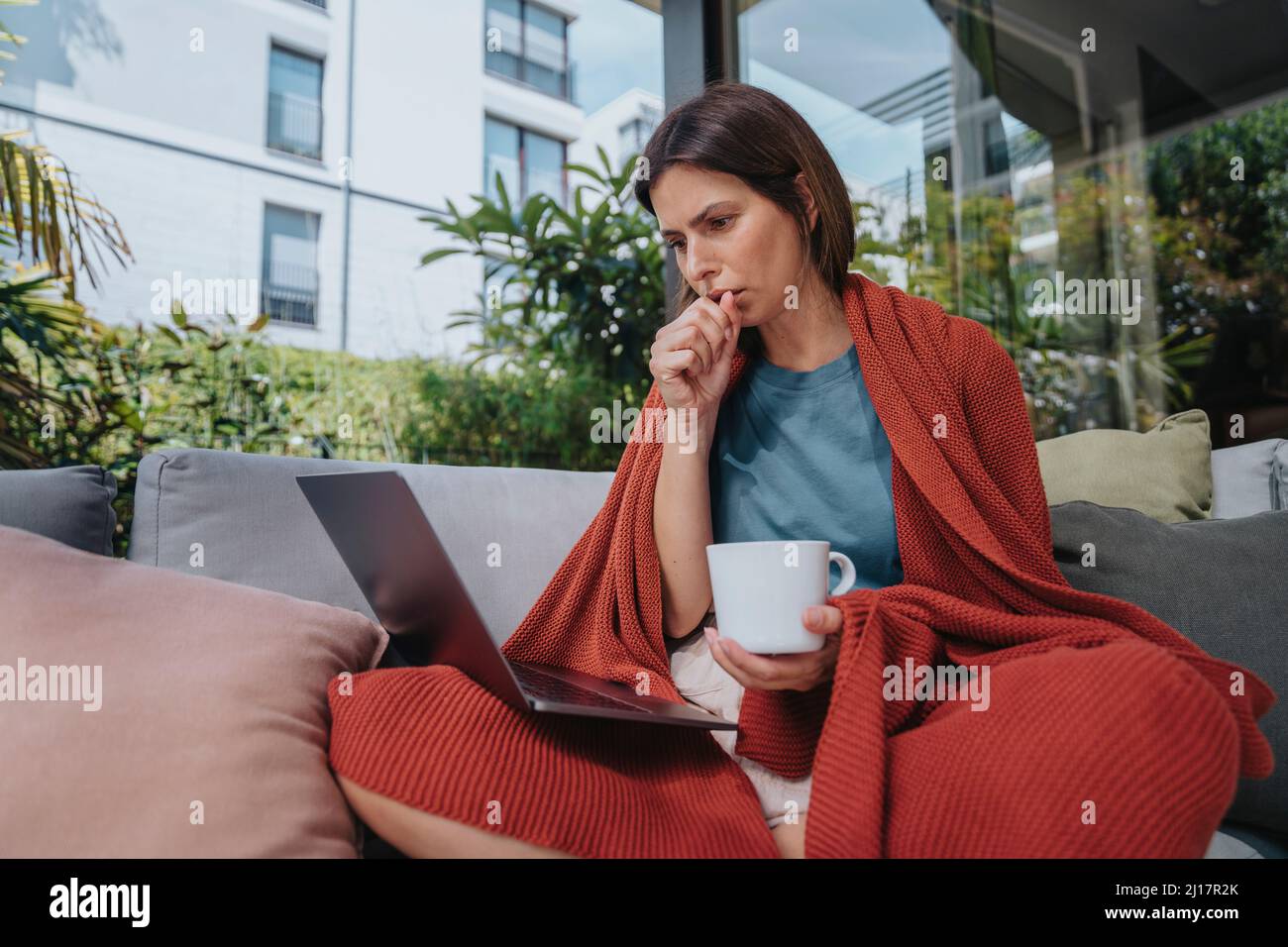 Sick businesswoman coughing and working on laptop in yard Stock Photo