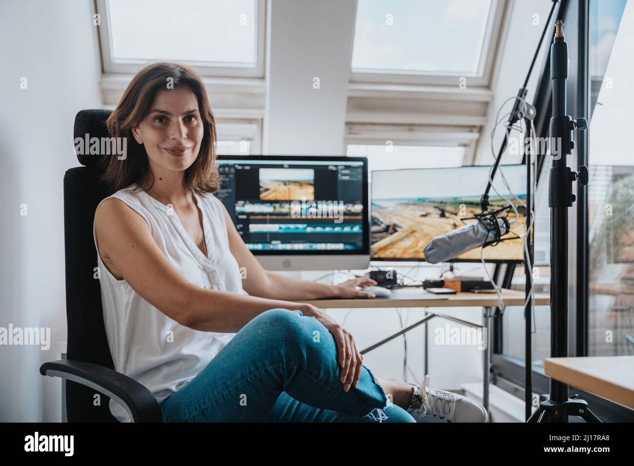 Photographer sitting on chair in front of desktop PC in studio Stock Photo