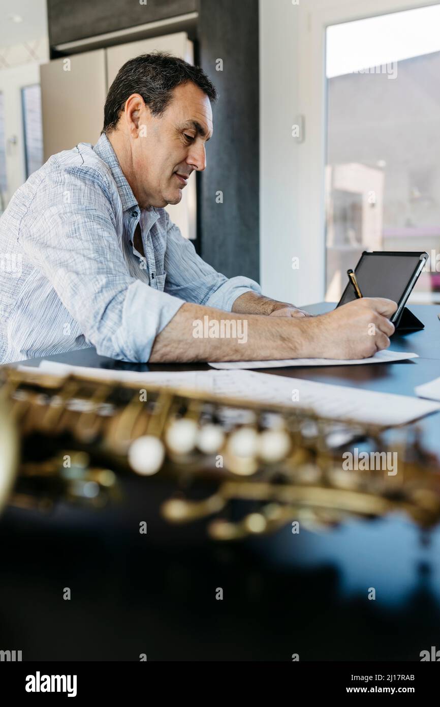 Saxophonist writing musical notes by tablet PC on table at home Stock Photo