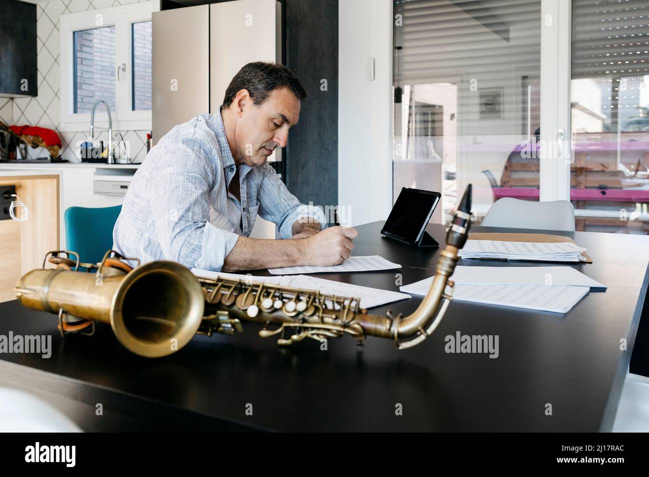 Saxophonist writing musical notes siting in kitchen at table Stock Photo