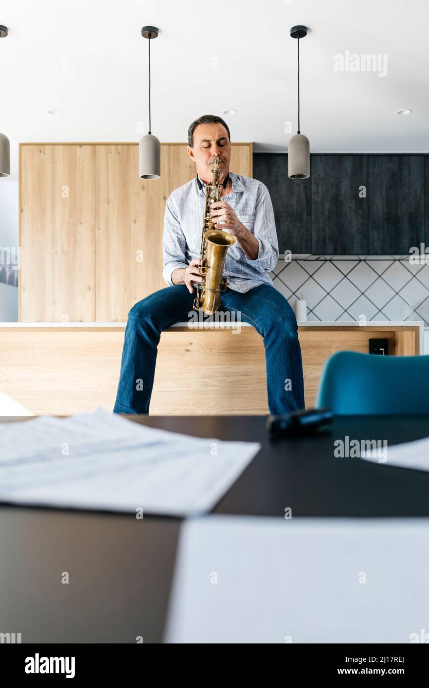Saxophonist practicing saxophone sitting on kitchen island at home Stock Photo