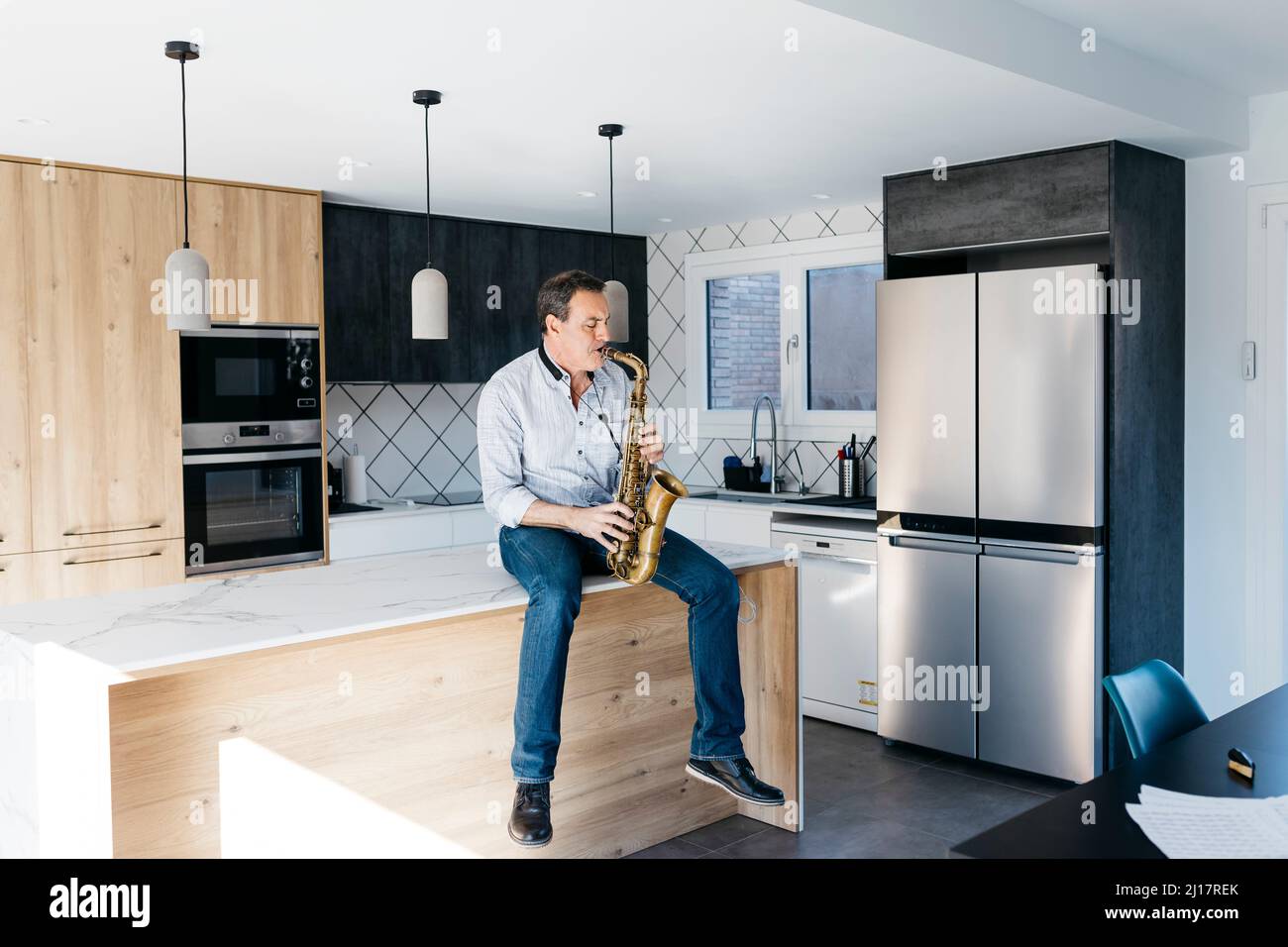 Musician playing saxophone sitting on kitchen island at home Stock Photo