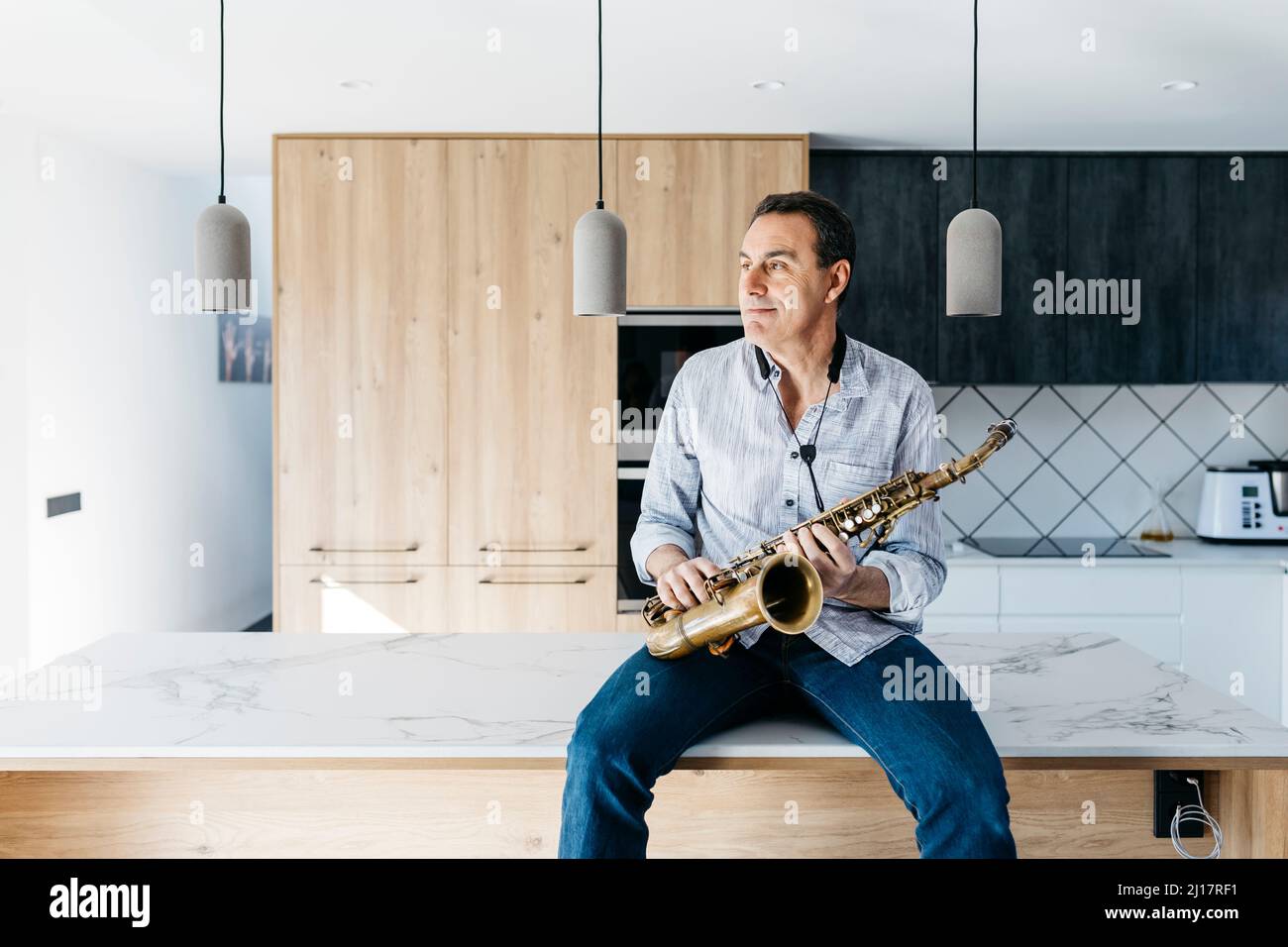 Saxophonist with saxophone sitting on kitchen island at home Stock Photo
