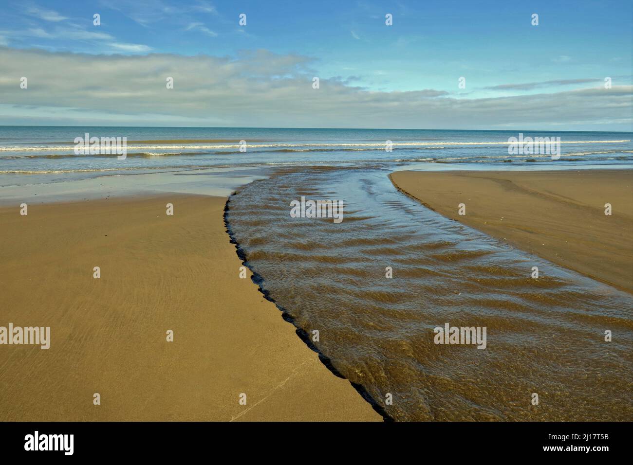 Colour photograph of the fast running river Hoffnant in spring across the sands to sea with varying textures and colours on the National Trust owned Stock Photo