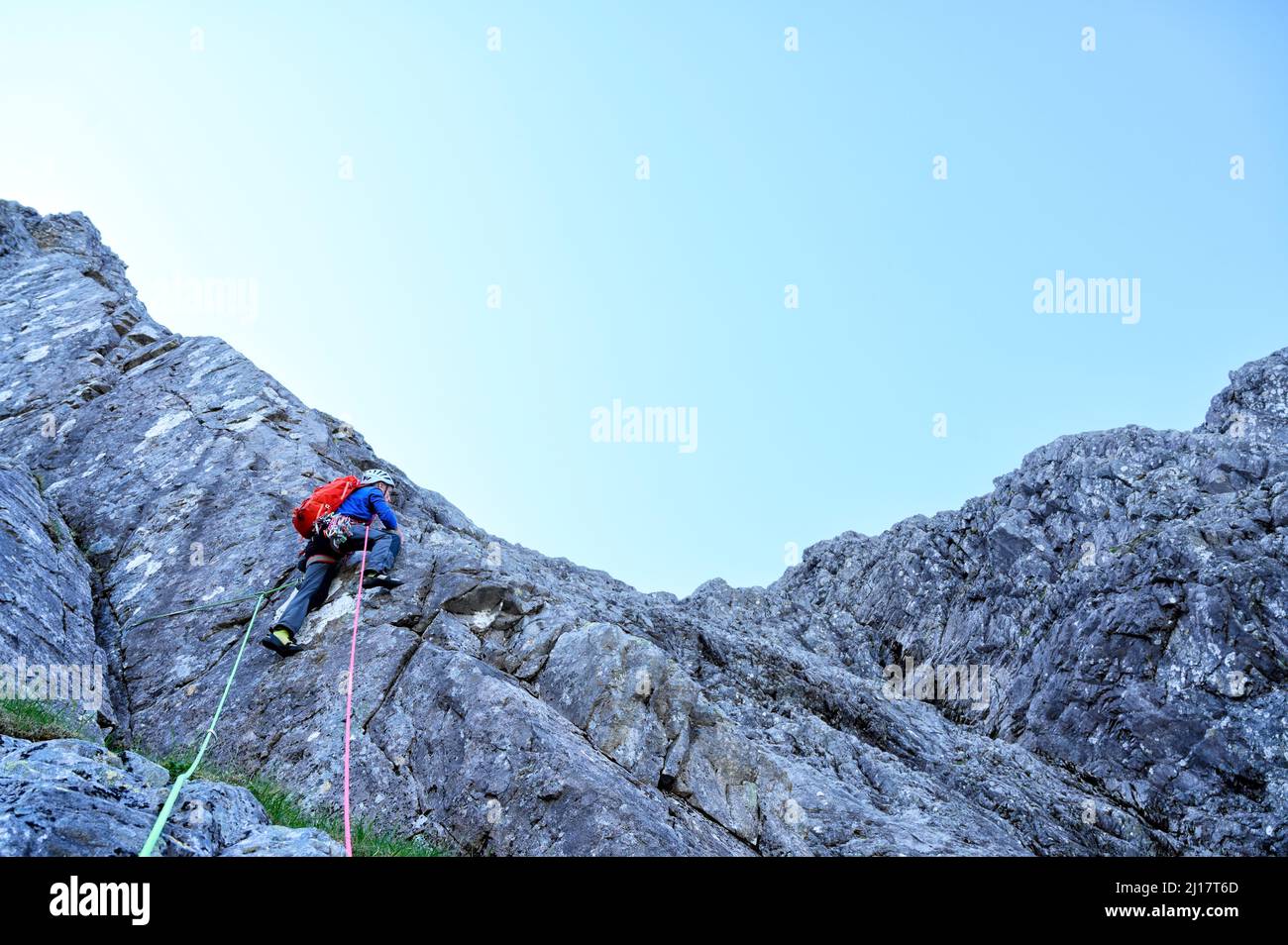 Man with rope climbing rocky mountain Stock Photo