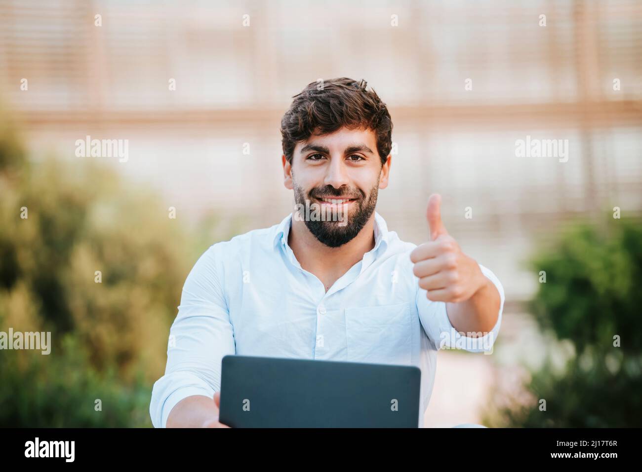 Smiling freelancer with laptop gesturing thumbs up Stock Photo