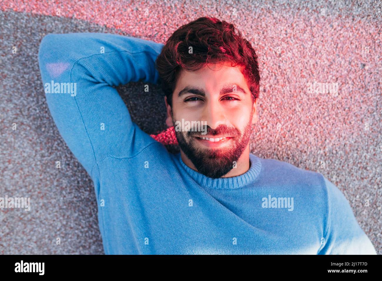Smiling young man with hand behind head lying on back Stock Photo