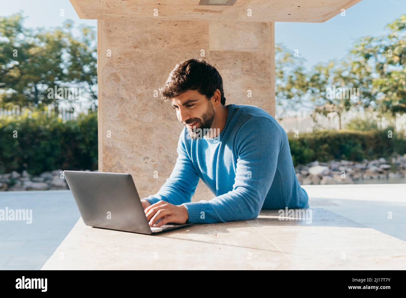 Smiling young man using laptop leaning on wall Stock Photo