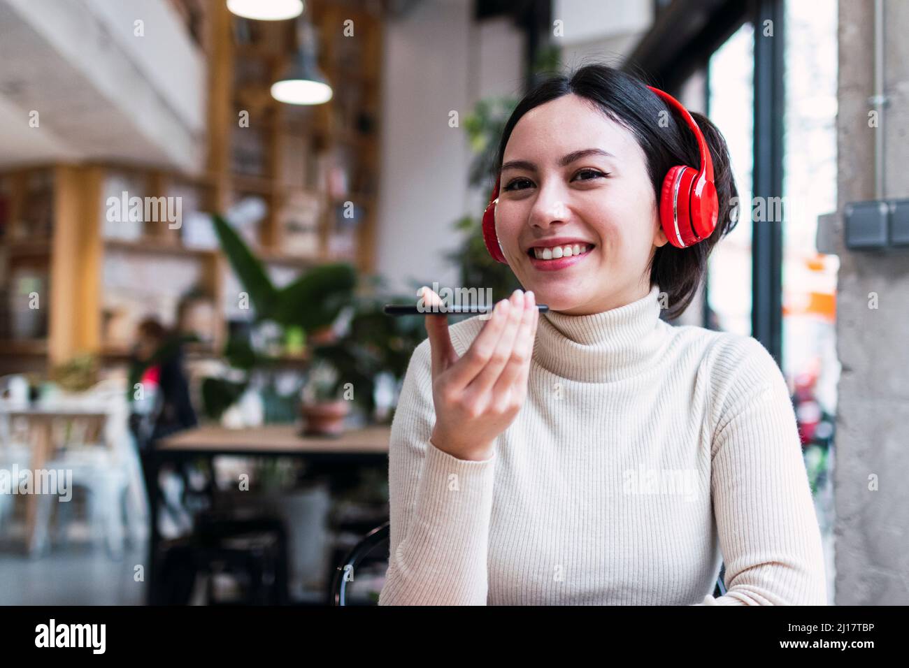 Happy woman wearing wireless headphones talking on mobile phone through ...