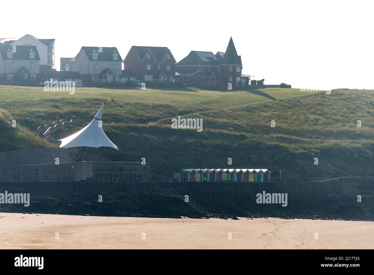Houses and beach huts on Nell's Point overlook the deserted sandy beach at Whitmore Bay, Barry Island early in the morning on a sunny day. Stock Photo