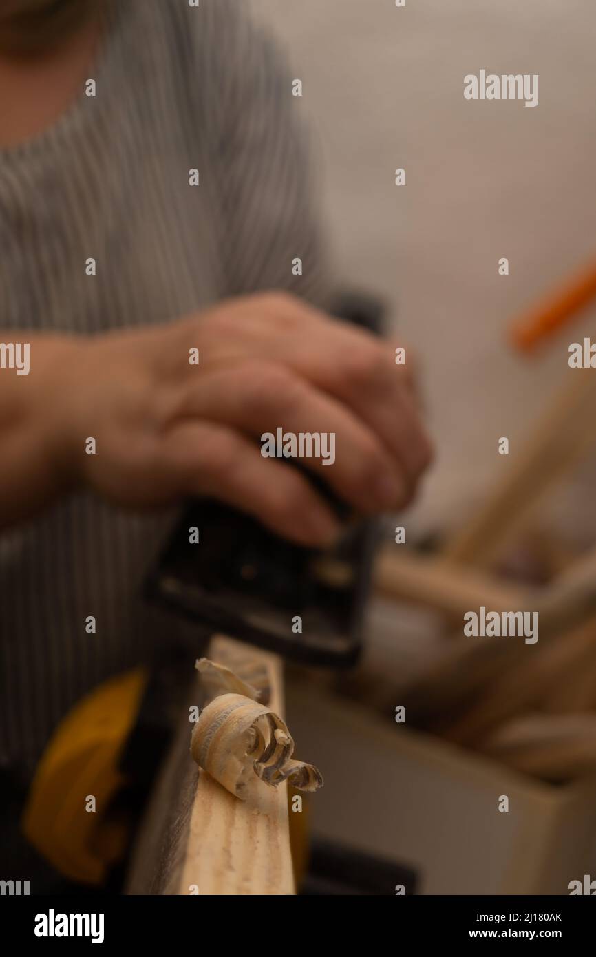 outoffocus closeup of a woman's hands planing wood with a hand
