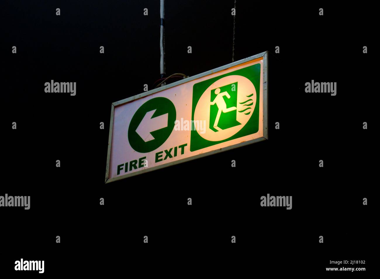 A fire exit sign hanging from a ceiling isolated on a black background