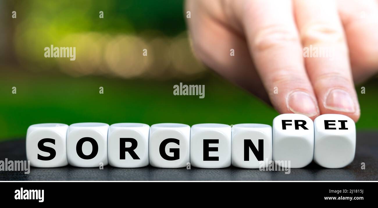 Hand turns dice and changes the German word 'Sorgen' (worries) to 'sorgenfrei' (carefree). Stock Photo
