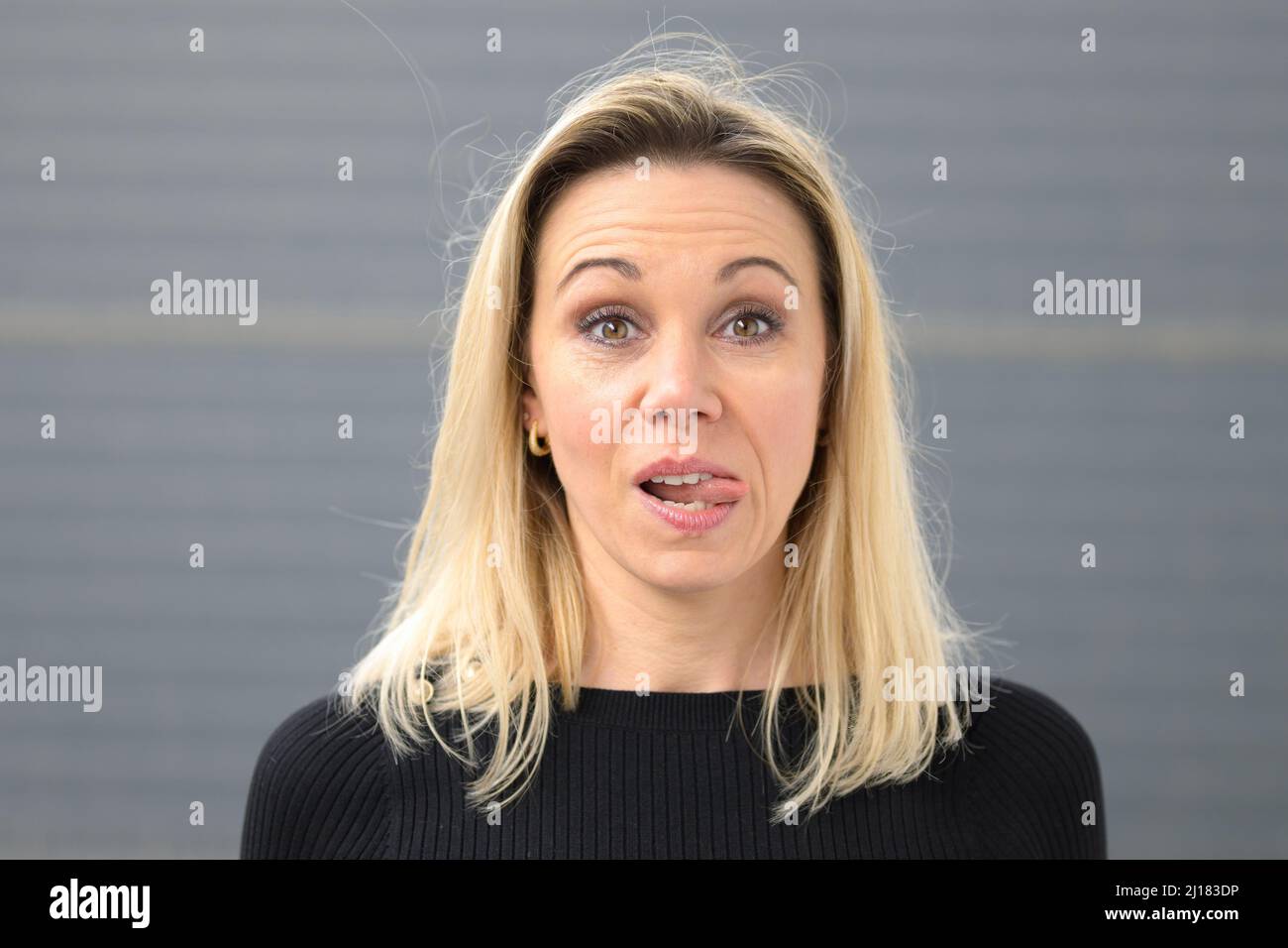 Head and shoulders portrait of pretty young blond woman with tongue out ...