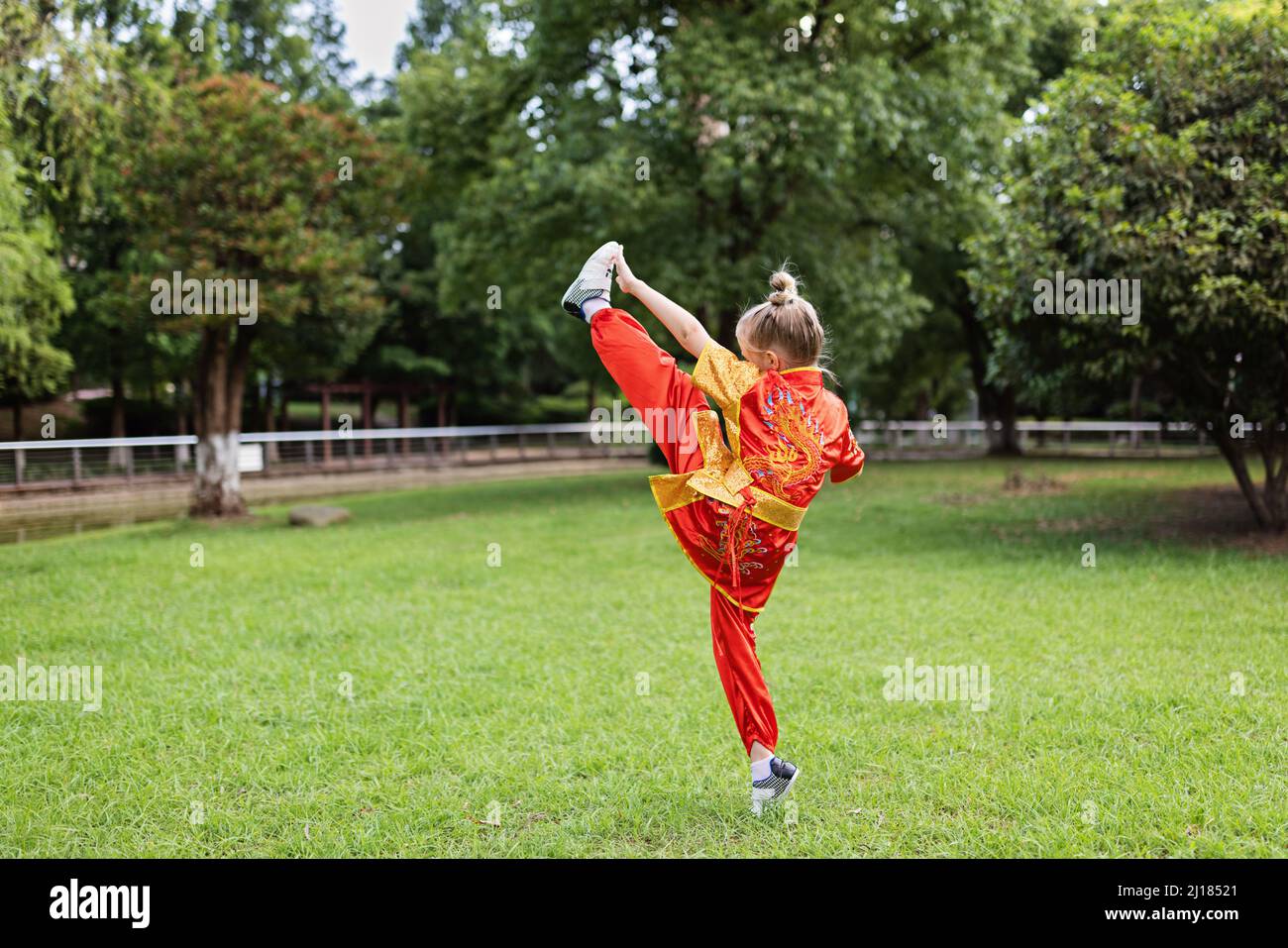 Cute little caucasian girl seven years old in red sport wushu uniform exercising in park at summer day. Lifestyle portrait of kung fu fighter child Stock Photo