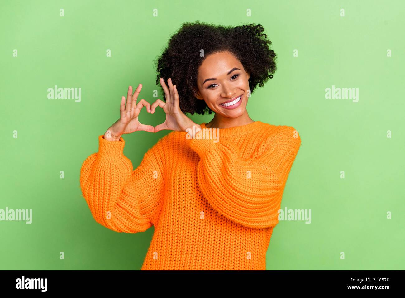 Photo of sweet millennial curly hairdo lady show heart wear orange pullover isolated on green color background Stock Photo