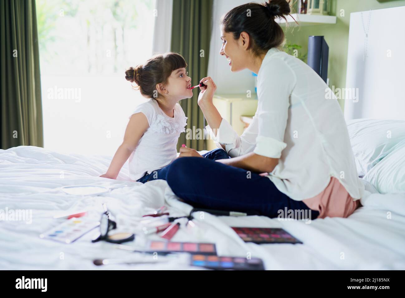 Now we both look exactly the same. Shot of a mother and her little daughter playing with makeup on the bed at home. Stock Photo