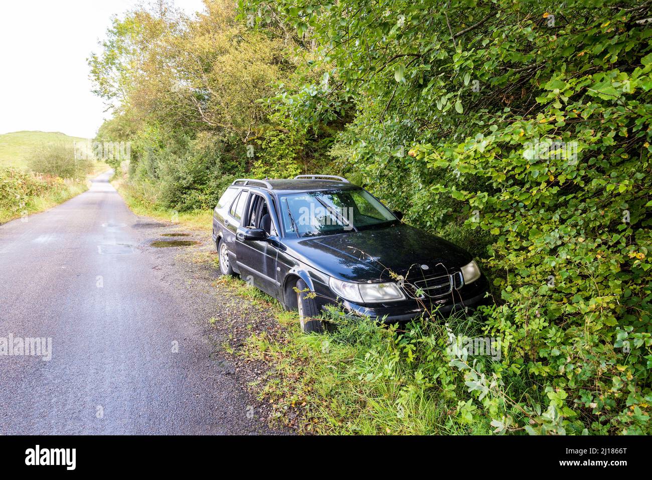 An abandoned vehicle, a black Saab estate, is left beside a quiet coutry lane on the island of Lismore in Scotland. Stock Photo