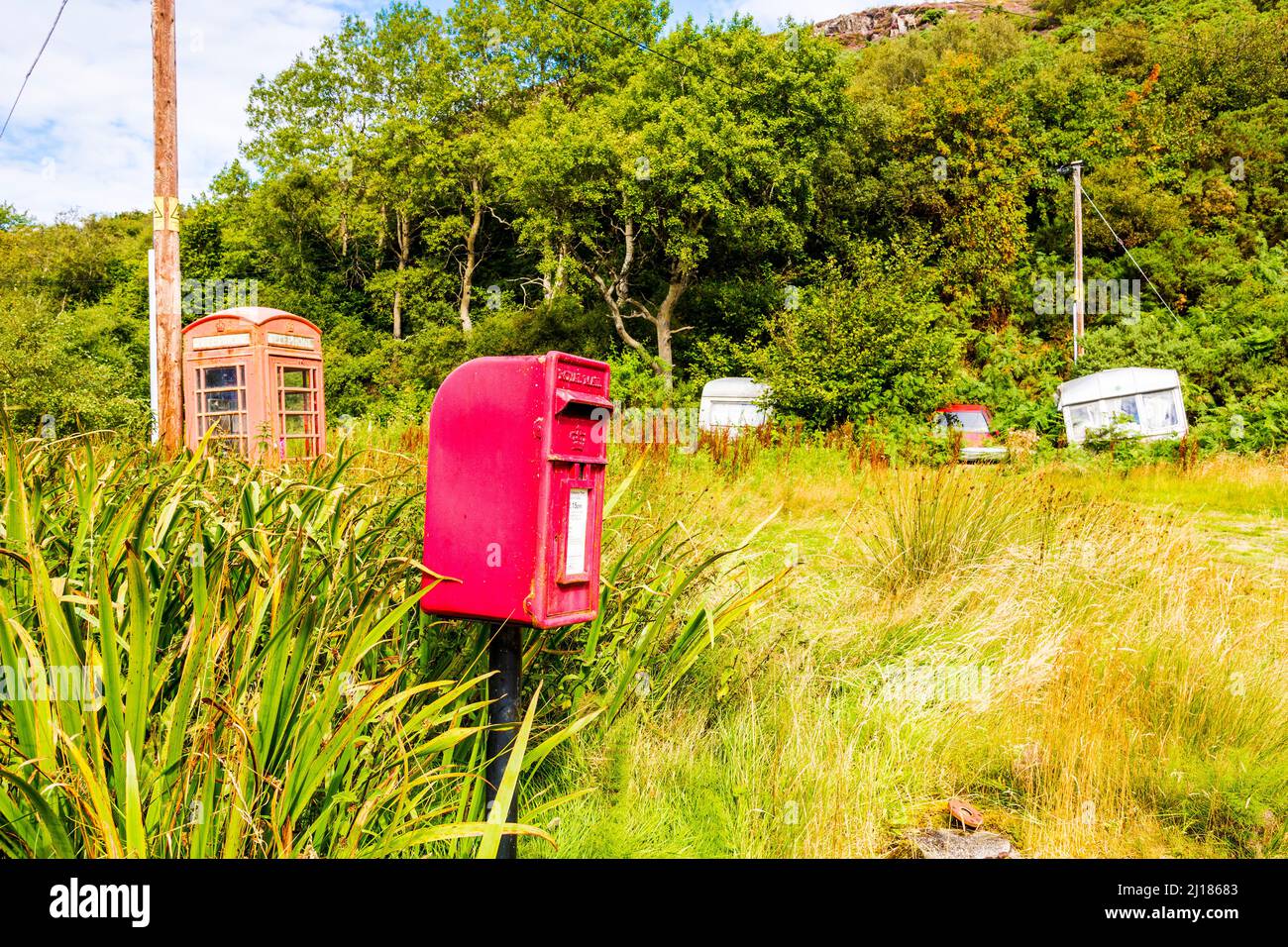 In the countryside, a letter box on a pole sits in front of an old phone box and an abandoned car and caravans near Torrisdale in Scotland. Stock Photo