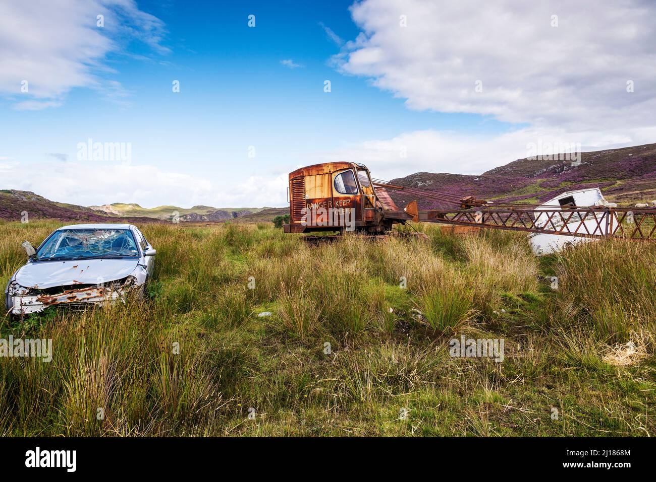 A smashed car, an old crane and an old boat sit abandoned in the countryside near Skerray in Scotland. Stock Photo