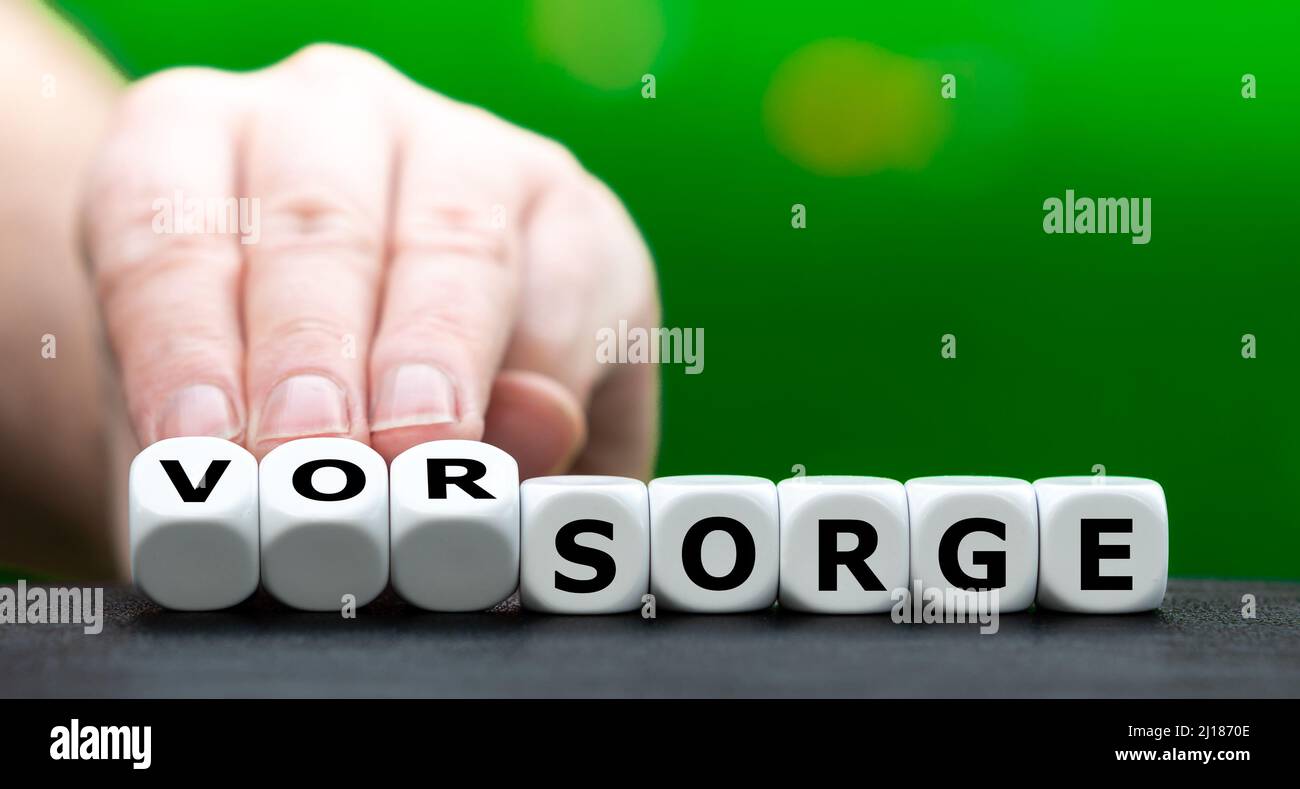 Hand turns dice and changes the German word 'Sorge' (worries) to 'Vorsorge' (medical check up). Stock Photo