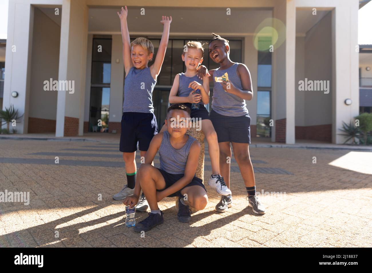 Cheerful elementary schoolboys against school building during sunny day Stock Photo