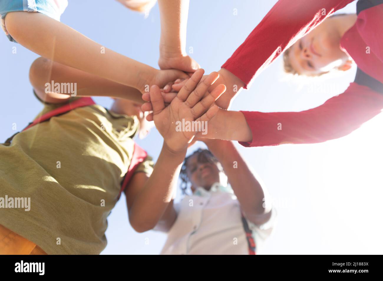 Directly below shot of multiracial elementary schoolboys stacking hands against sky during sunny day Stock Photo