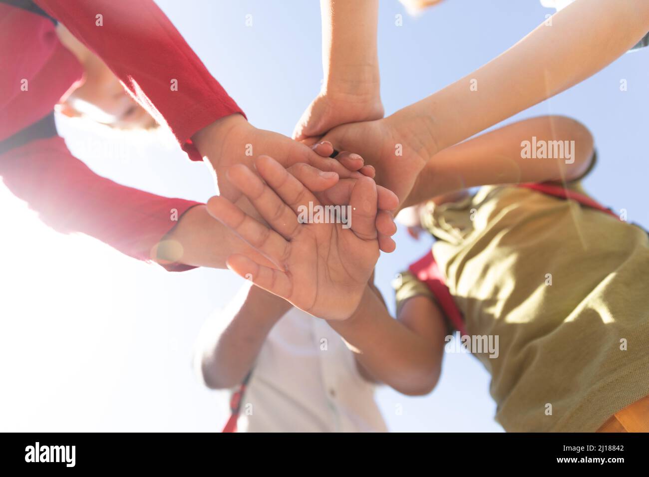 Directly below shot of multiracial elementary schoolboys stacking hands while standing against sky Stock Photo