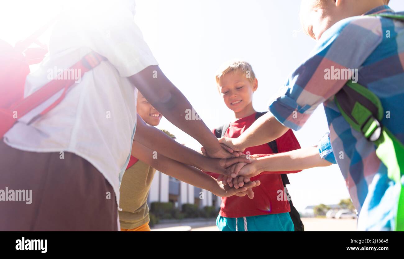 Happy multiracial schoolboys stacking hands while standing in school campus Stock Photo