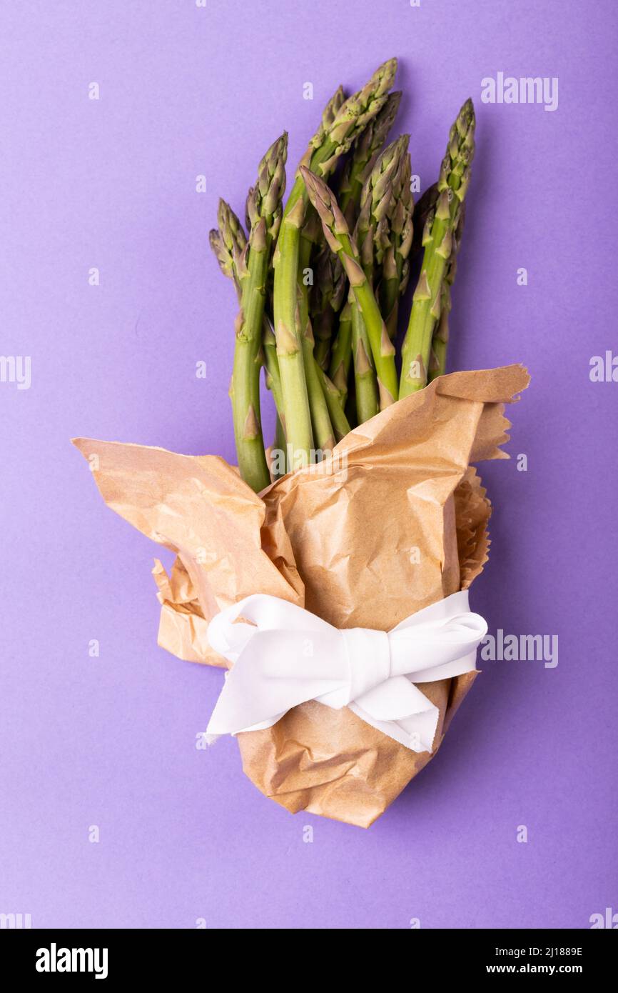 Directly above view of asparagus bunch in brown paper tied with white ribbon on purple background Stock Photo