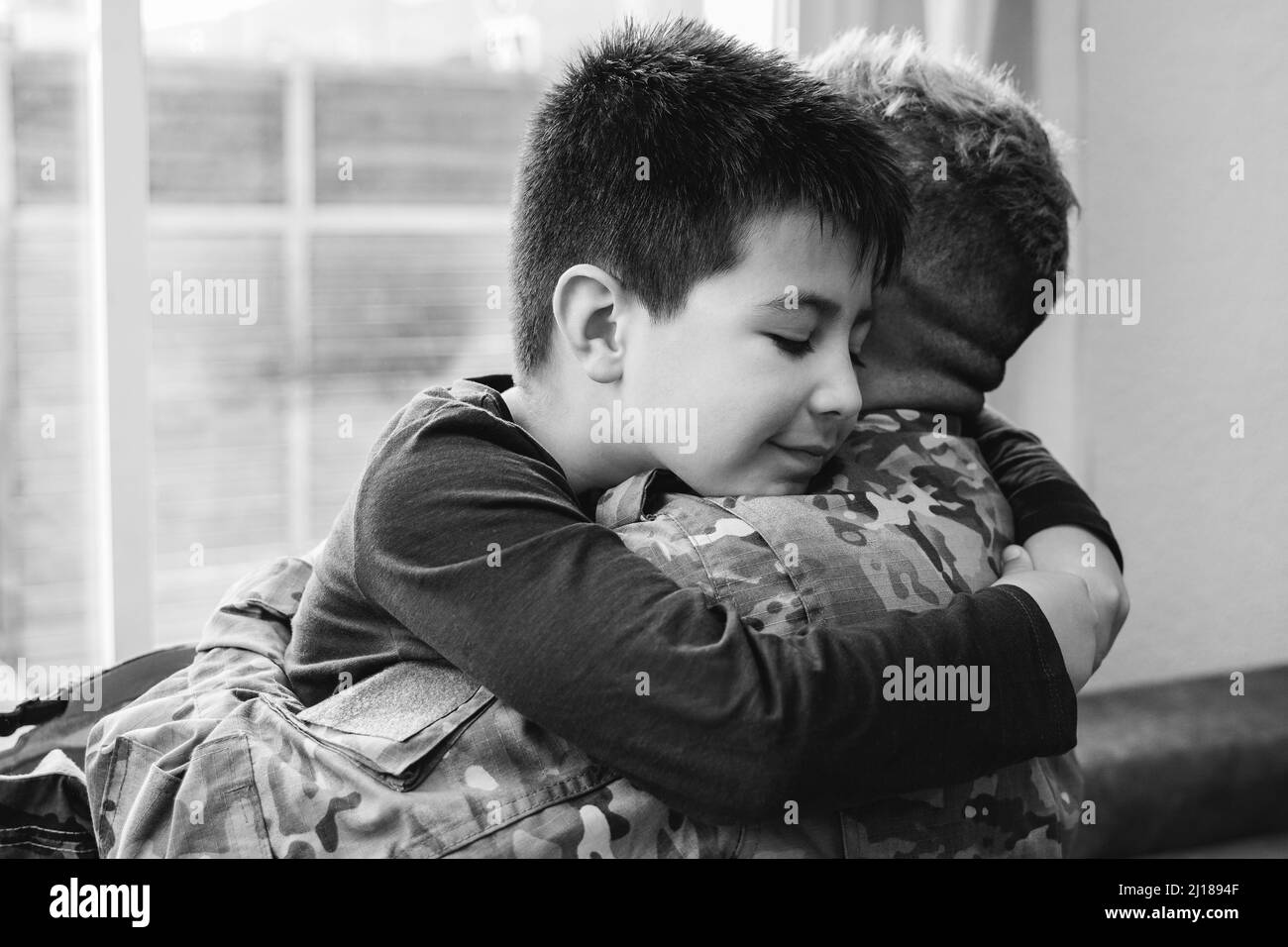 Veteran father hugging his kid son after homecoming reunion - Family love and war concept - Focus on child face - Black and white edition Stock Photo