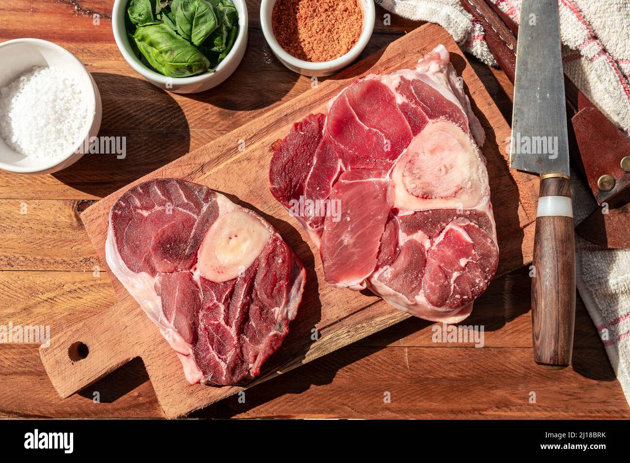 Two steaks of raw beef ossobuco on a wooden board with seasoning to flavour the pieces of meat. Animal protein concept, cheap cuts of beef. Aereal vie Stock Photo