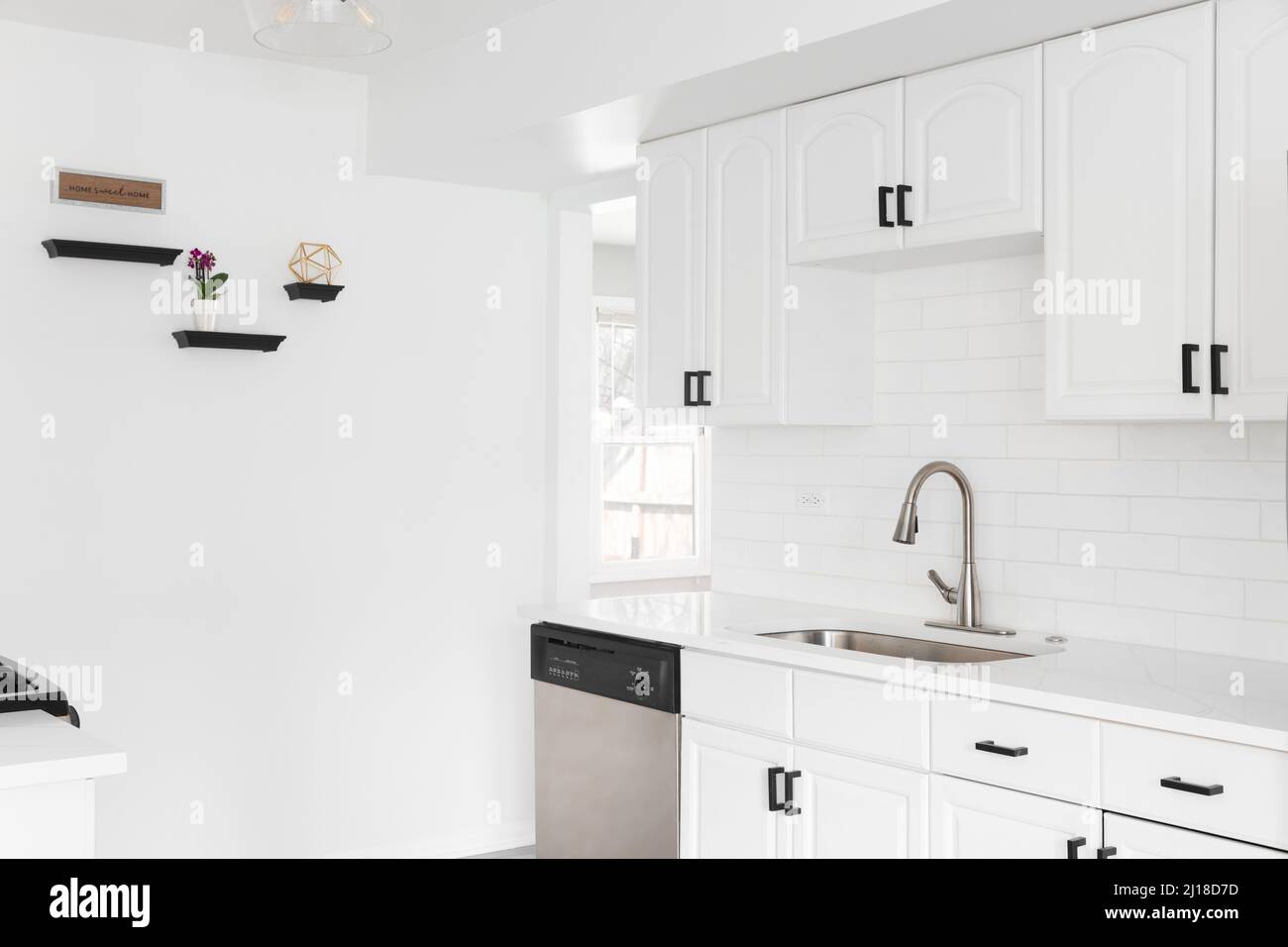 A bright kitchen with white cabinets, subway tile backsplash, black hardware, and a stainless steel sink. Stock Photo