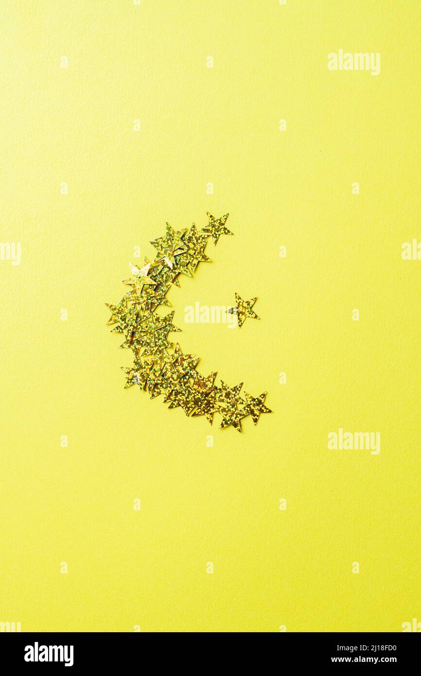Shape of moon from glowing glitters. Yellow background and top view. Stock Photo
