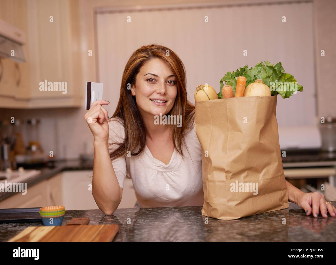 Shes a satisfied shopper. Portrait of a young woman standing with a credit card and groceries. Stock Photo