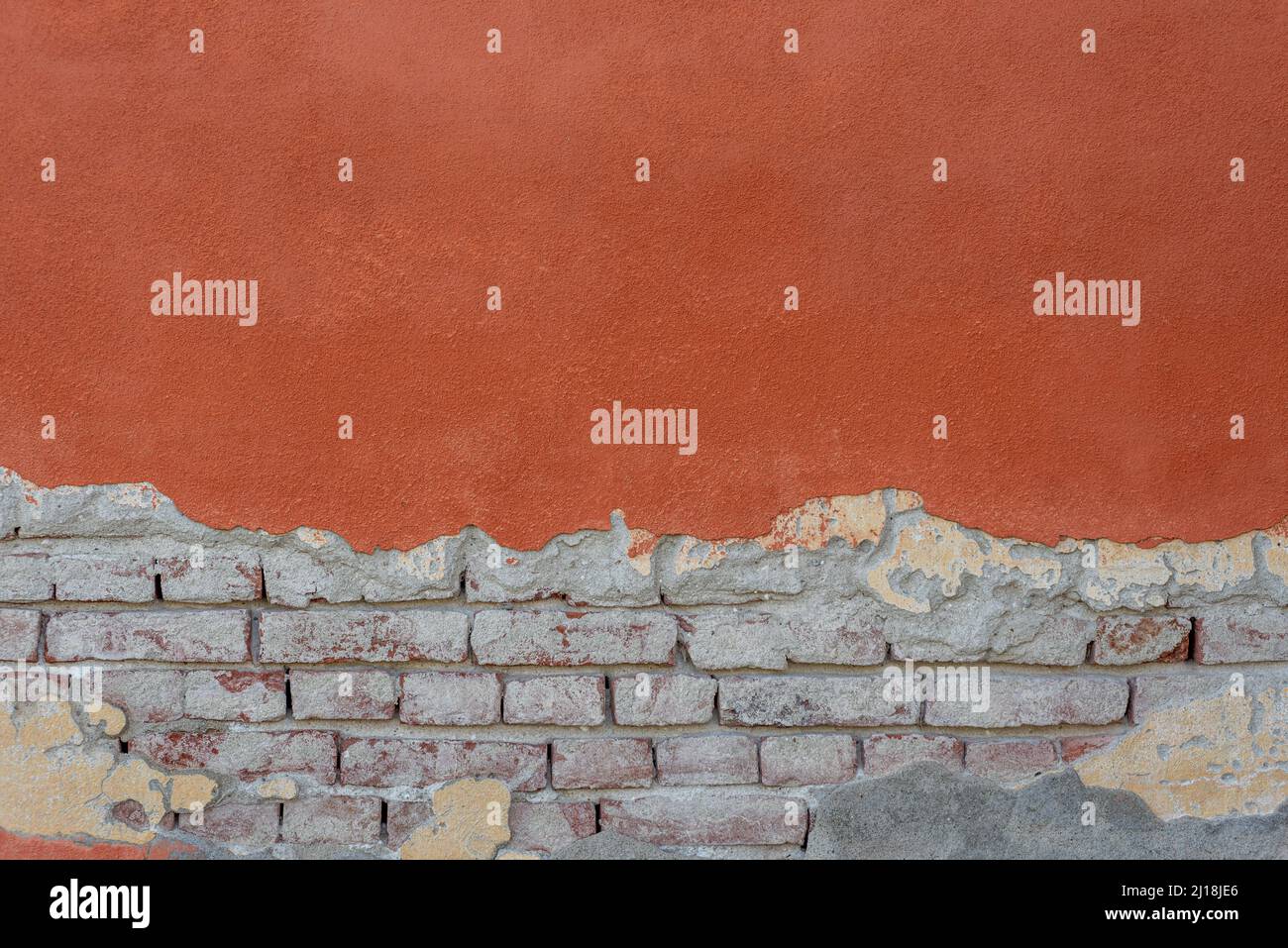 Wall texture with red plaster and peeling bottom with exposed brick. Wall background with red plaster and brick with cement. Ideal for background with Stock Photo
