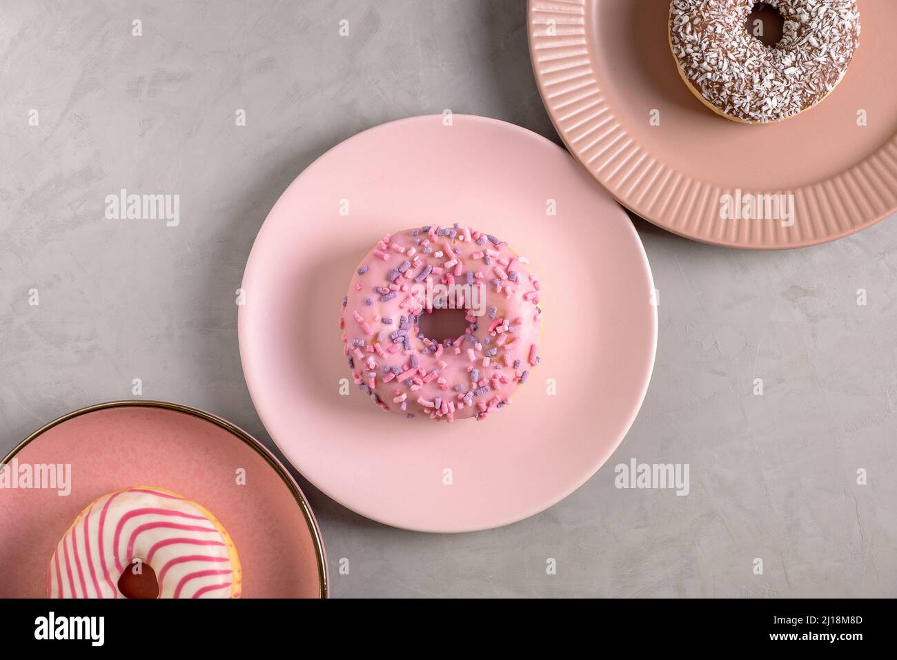 Three glazed donuts lie on tall pink plates Stock Photo