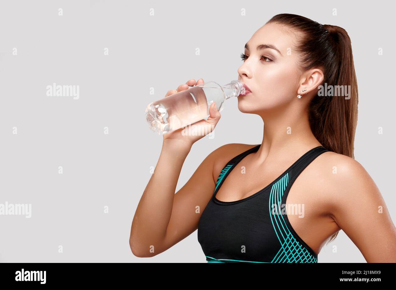 Strong sporty caucasian woman in black fitness suit drinks water on isolated gray background Stock Photo