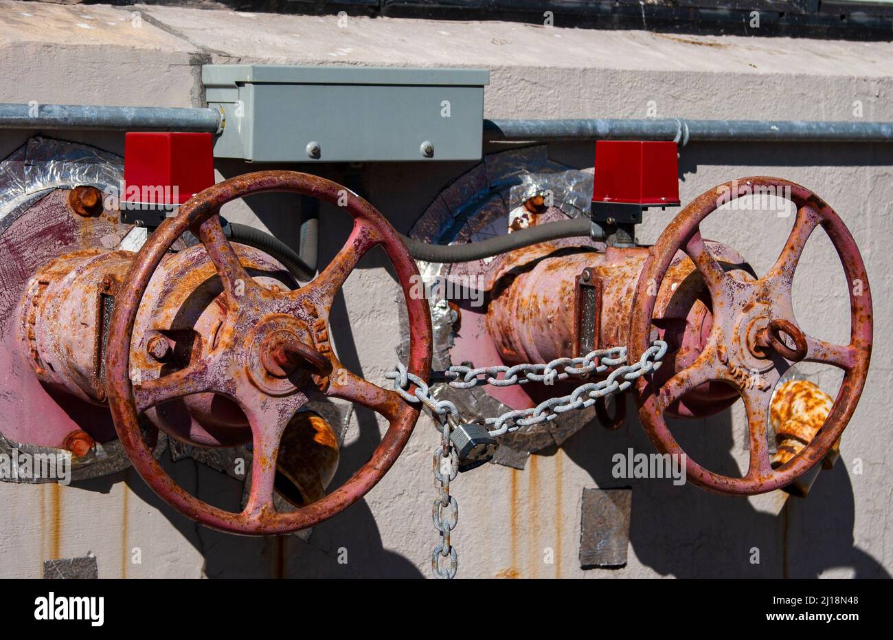 The photo shows two rusted shut-off valves in the sun secured by a lock Stock Photo