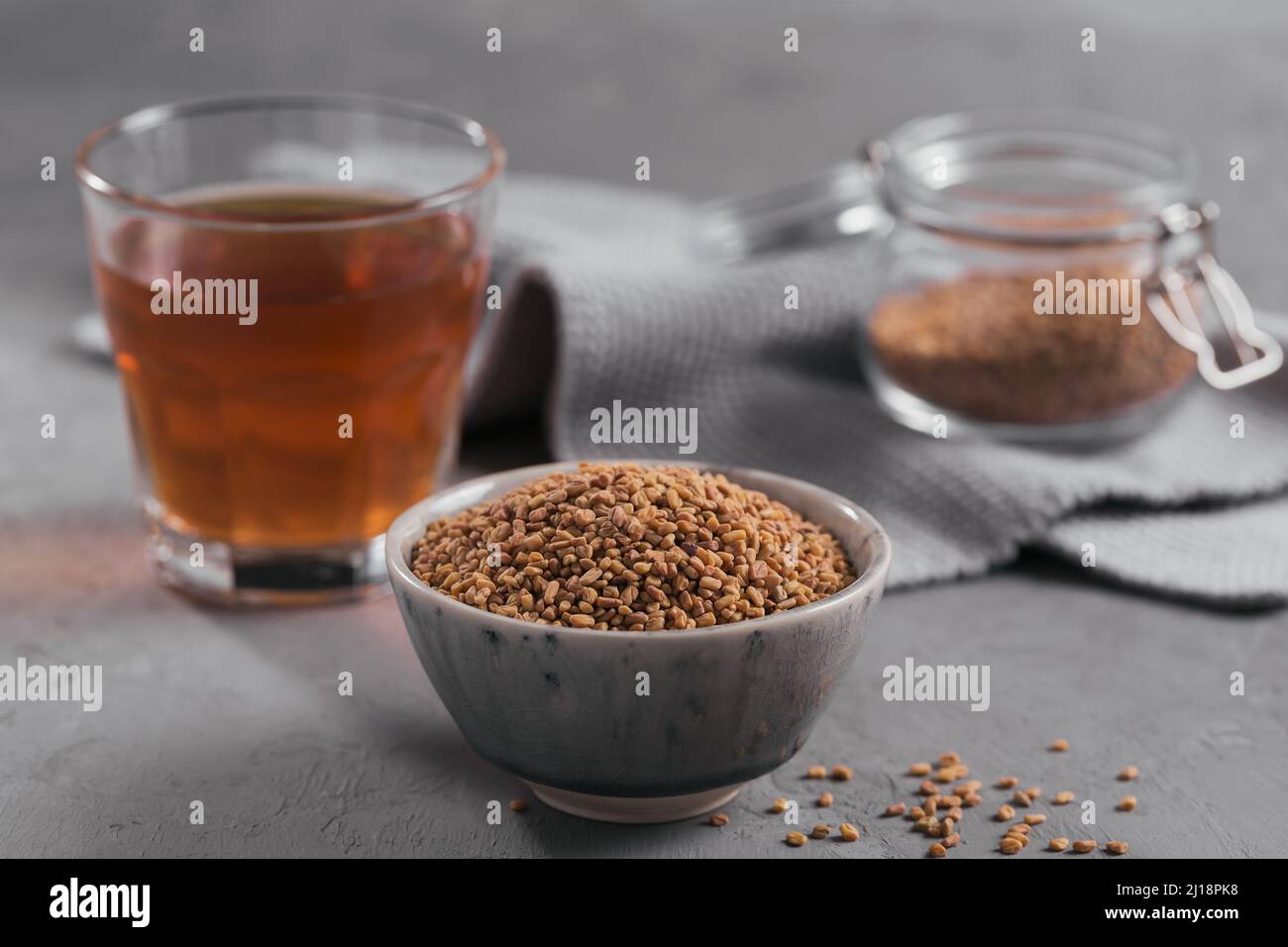 Bowl of fenugreek seeds and Egyptian fenugreek yellow tea or Methi Dana drink on grey background Stock Photo