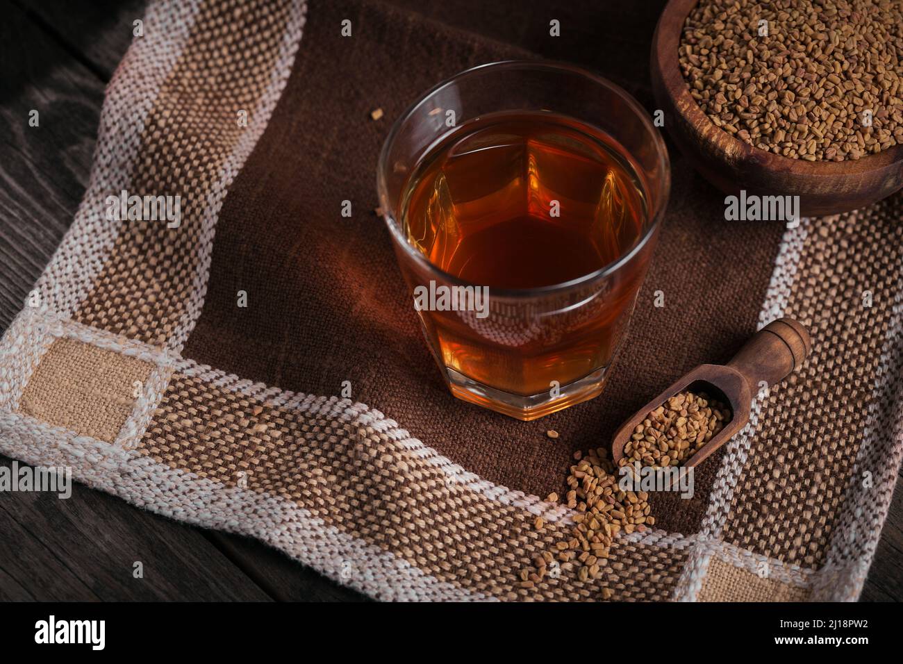 Glass of Egyptian fenugreek yellow tea, Helba or Methi Dana drink and fenugreek seeds on dark wooden background Stock Photo