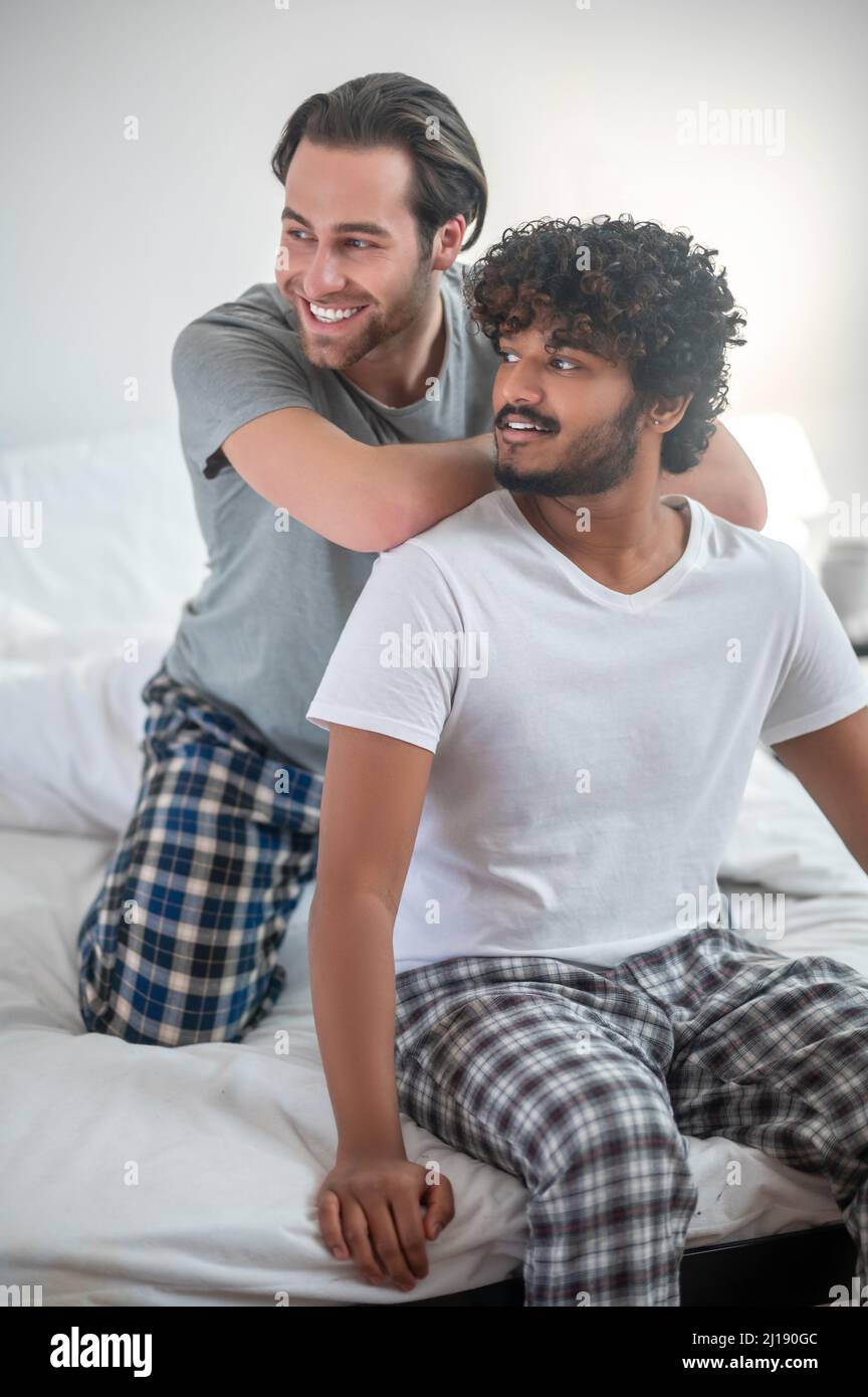 Young biracial gay couple in pajamas sitting on the bed Stock Photo