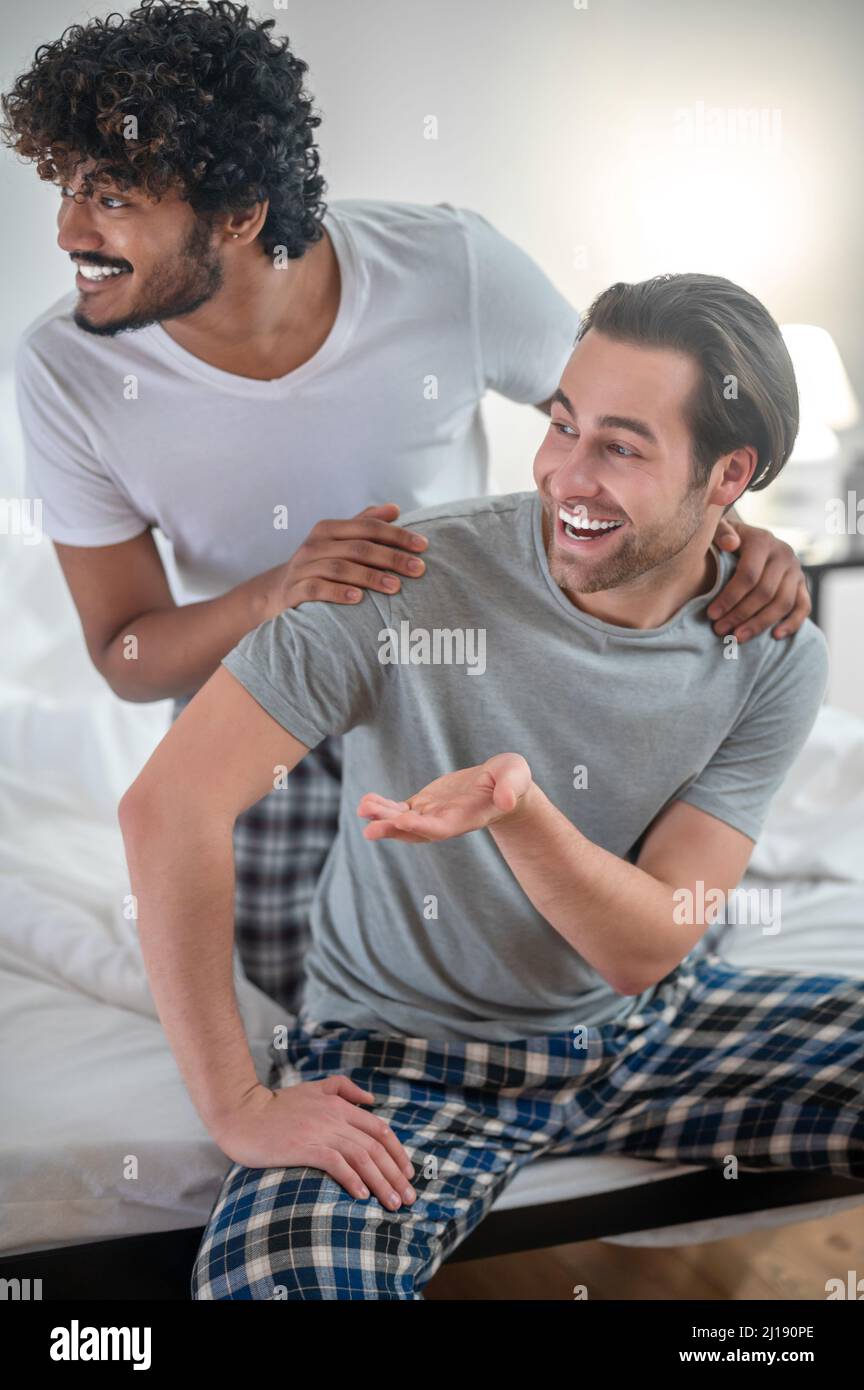 Cheerful biracial gay couple sitting in the bedroom Stock Photo