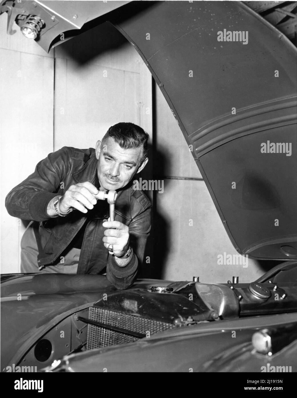 CLARK GABLE tinkers under the bonnet of his JAGUAR XK120 sports car in the garage at his Ranch Home in Encino California in 1950 publicity for Metro Goldwyn Mayer Stock Photo