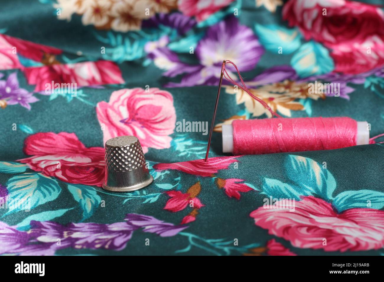 Thimble With Needle and Pink Thread on Vintage Floral Satin Fabric Green and Pink Stock Photo