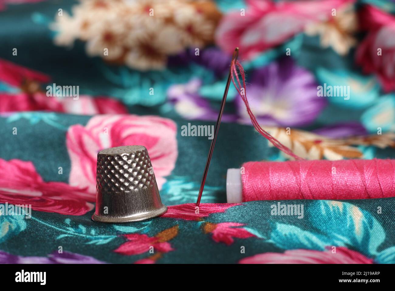 Thimble With Needle and Pink Thread on Vintage Floral Satin Fabric Green and Pink Stock Photo