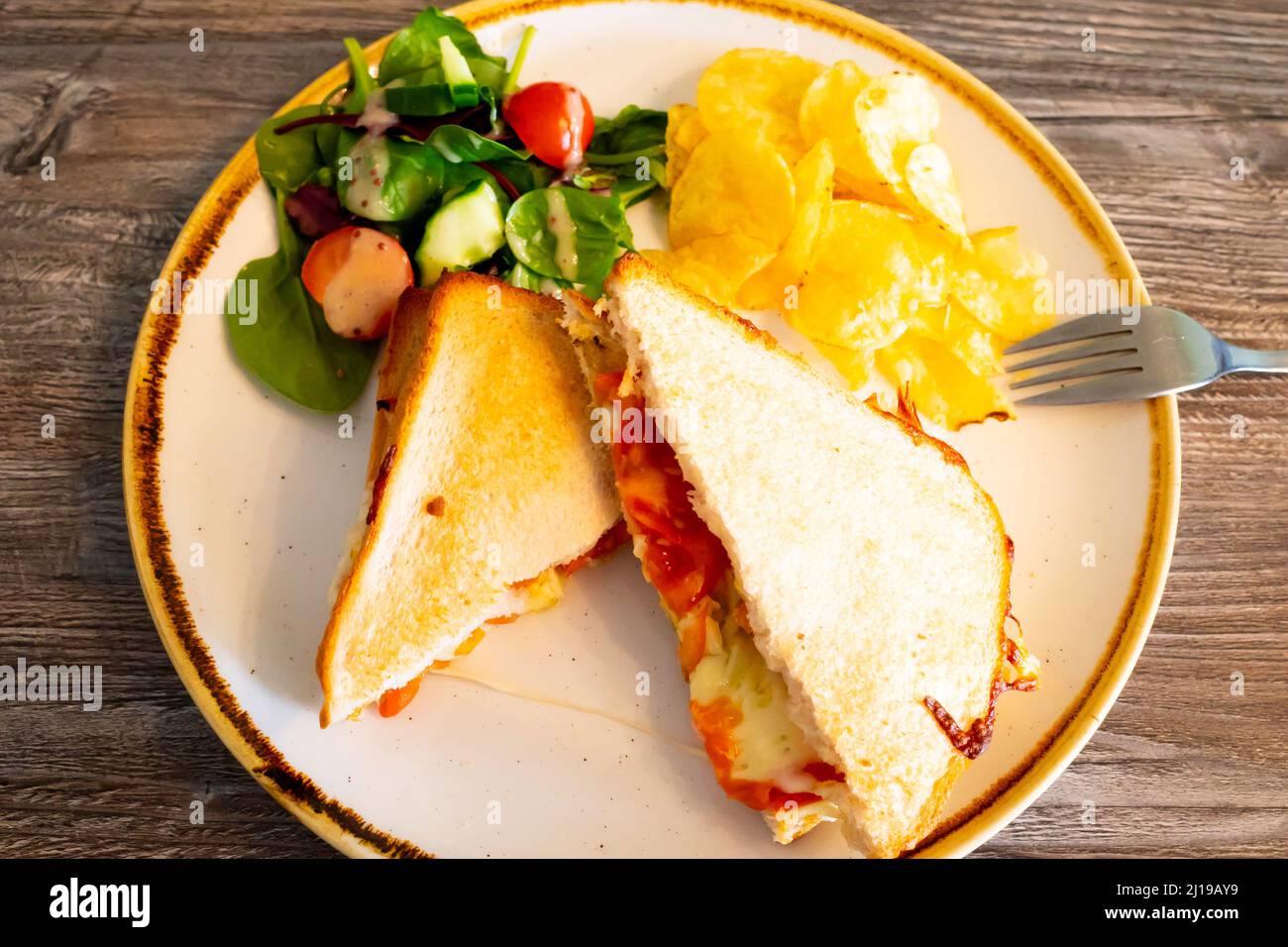 Lunch in a North Yorkshire country café  cheese and pepperoni  toasted sandwich on white bread with salad and potato crisps Stock Photo