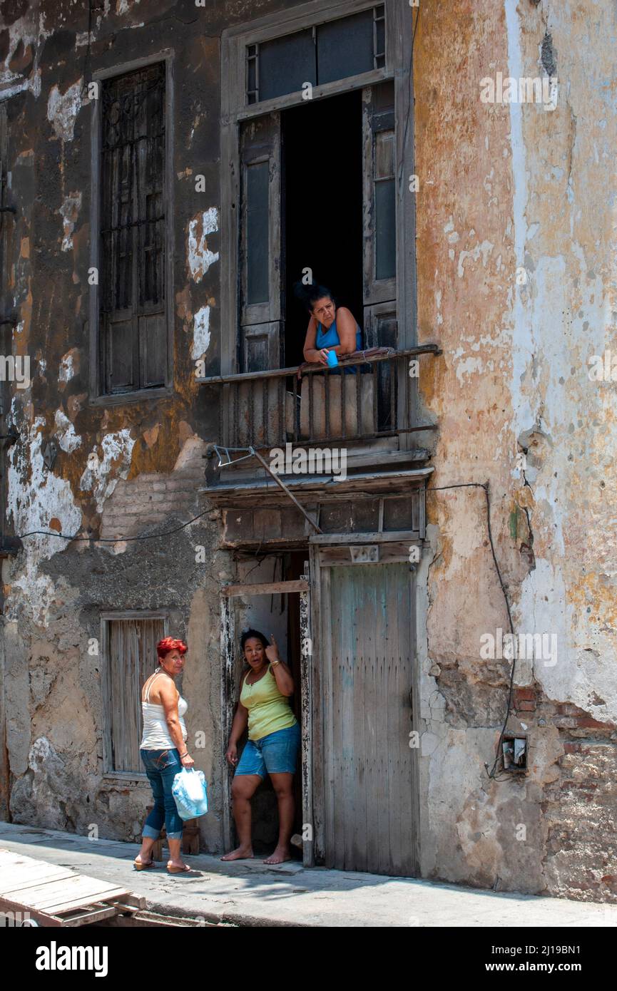 Cuban woman signals for one dollar for a photo while her woman and neighbor watch. Stock Photo