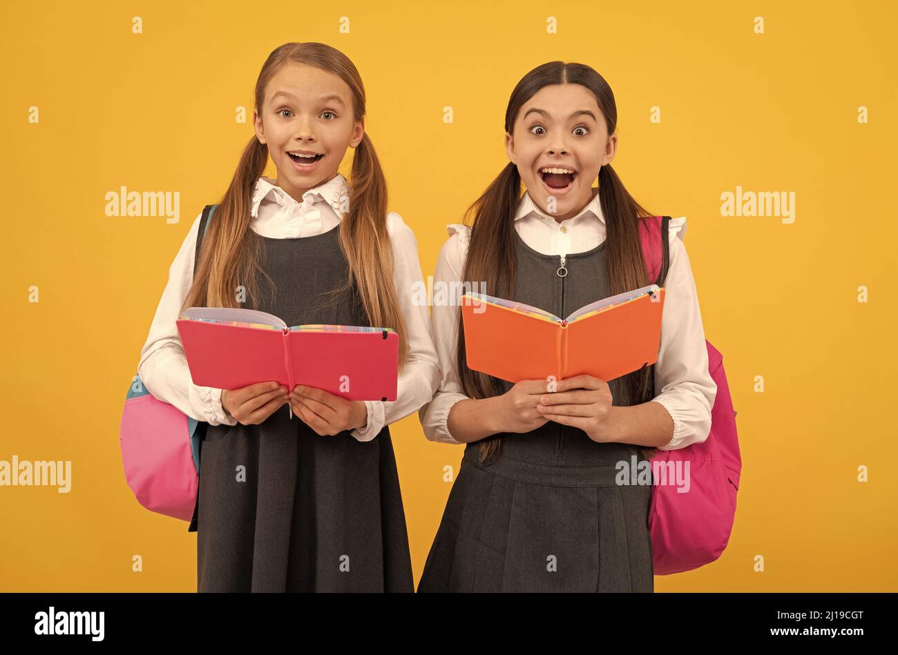 Surprised children in formal uniforms read school books yellow background, library Stock Photo